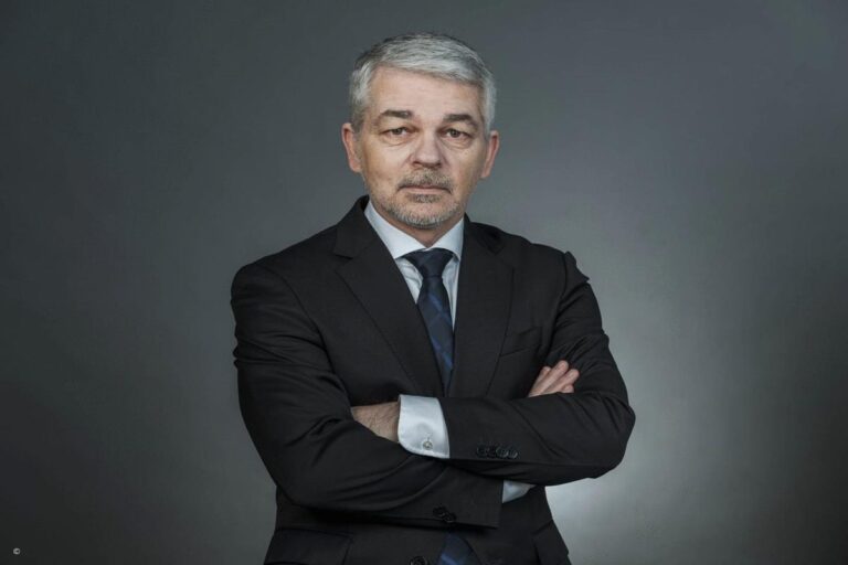 Carlo Masala im Anzug mit verschränkten Armen vor neutralem Hintergrund – Experte für internationale Politik
