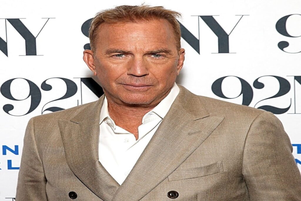 Kevin Costner bei einem Fototermin vor einer Pressewand, ernst und elegant im beigen Anzug