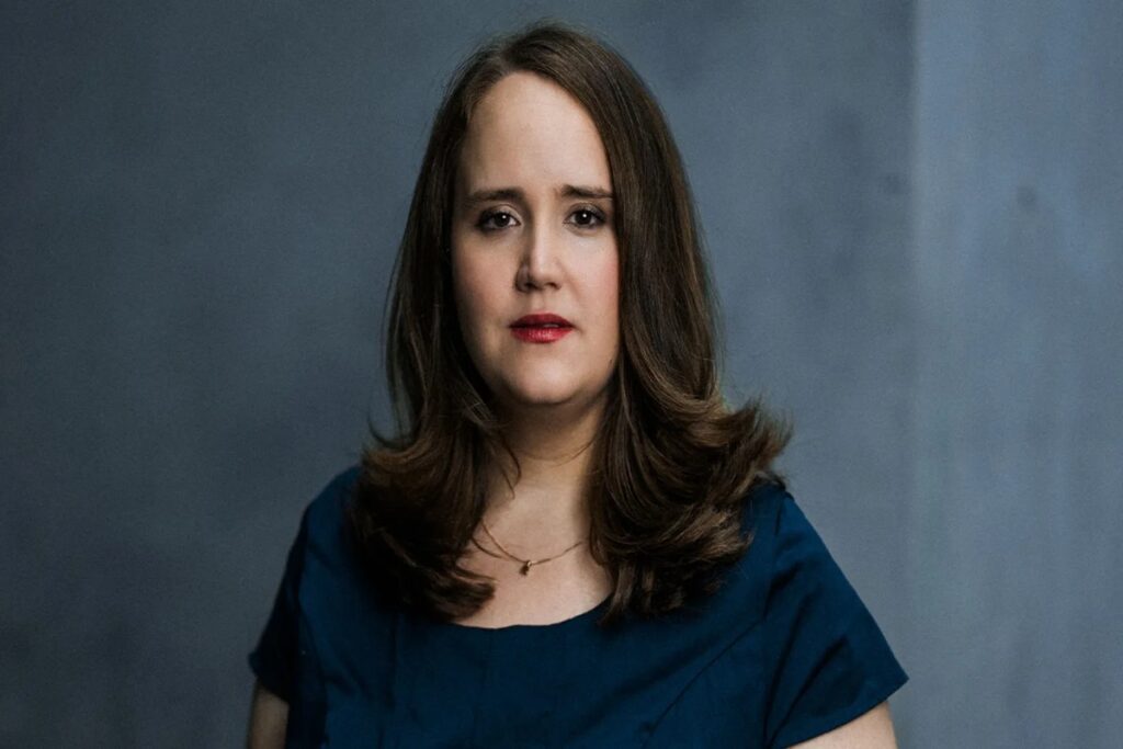 Ricarda Lang spricht auf einer politischen Bühne mit entschlossener Geste vor grünem Hintergrund